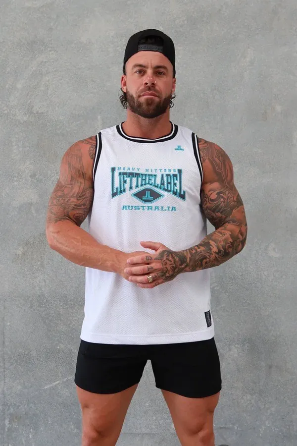 Man wearing a white and teal Lift The Label Heavy Hitters mesh jersey tank against a concrete wall