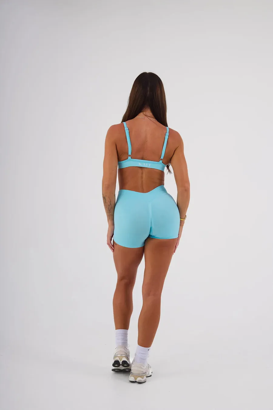 Woman wearing a Kali Activewear base bra and V-waist booty shorts in lagoon blue